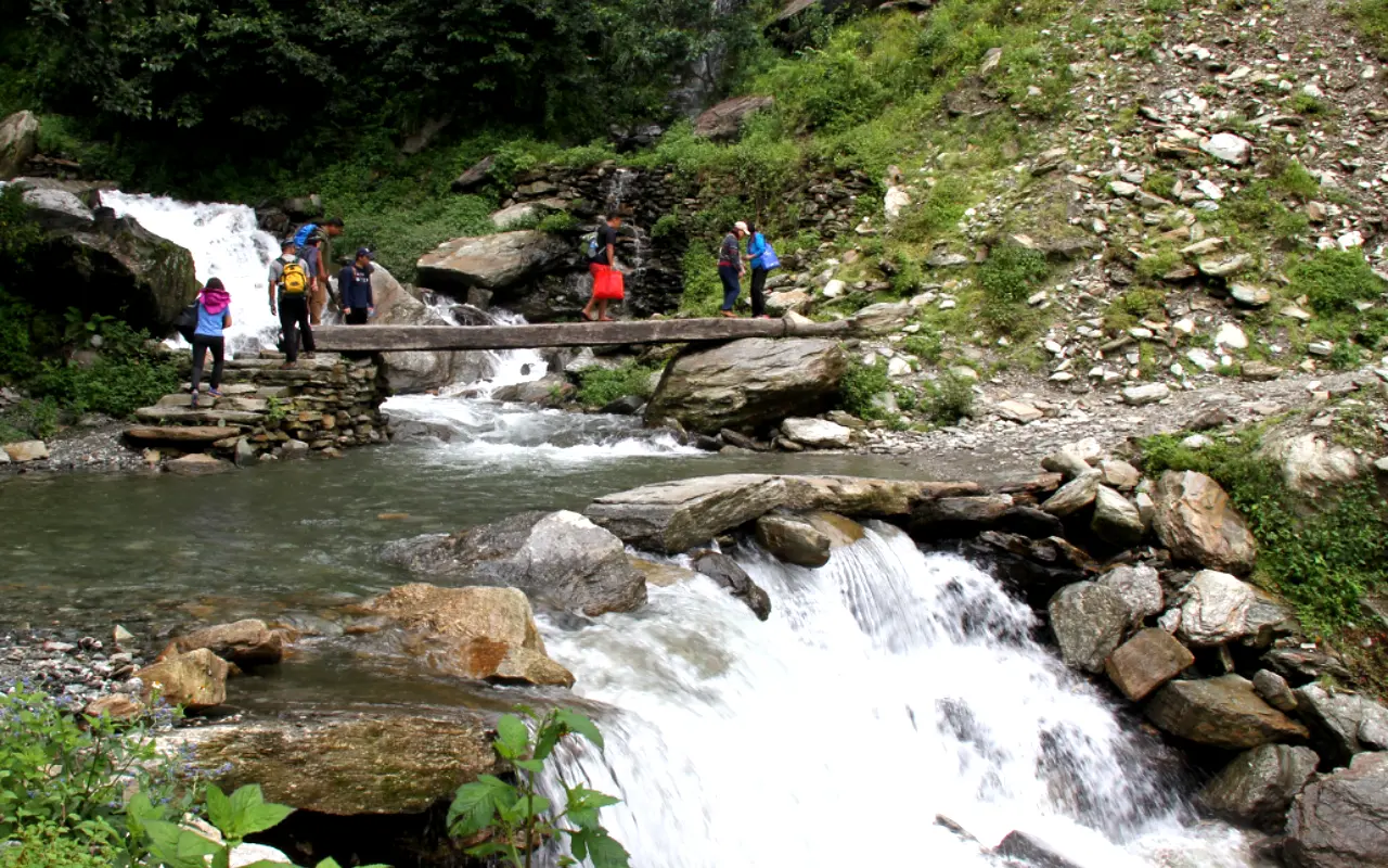 People crossing a man-made wooden bridge over the waterfalls in Ghandruk